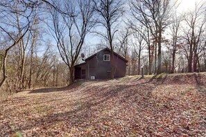 Eine rustikale Holzhütte mit geneigtem Dach, umgeben von bodenbedeckten Blättern und kahlen Bäumen.
