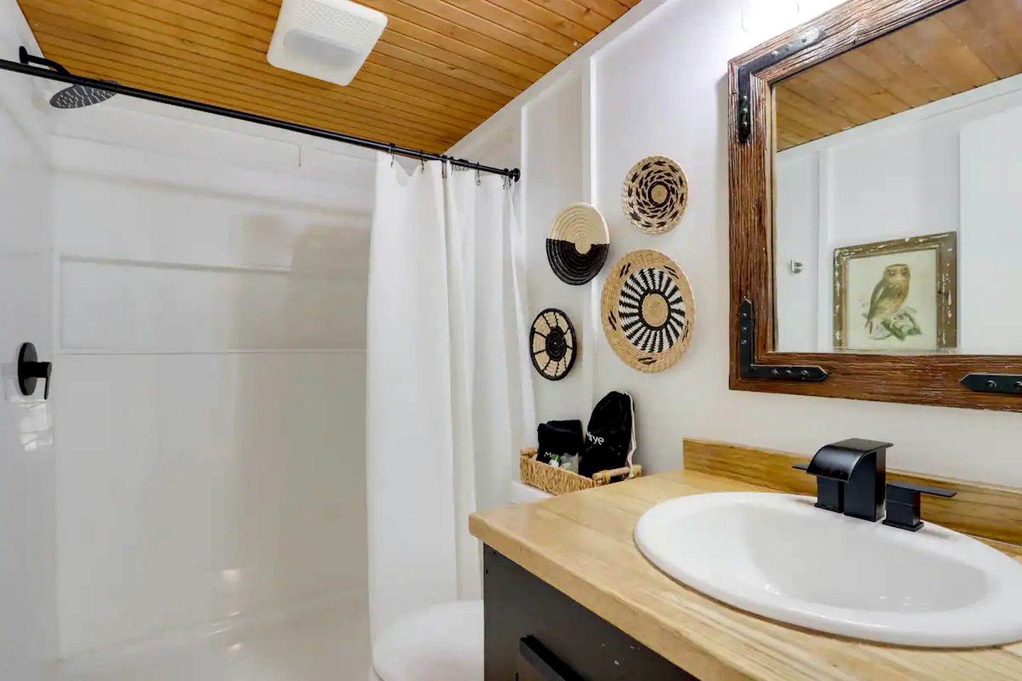 A bathroom with a wooden ceiling, a white sink, a mirror, and decorative wall plates.