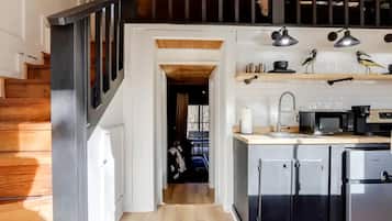 A kitchen with a wooden staircase, a microwave, a sink, and a refrigerator.