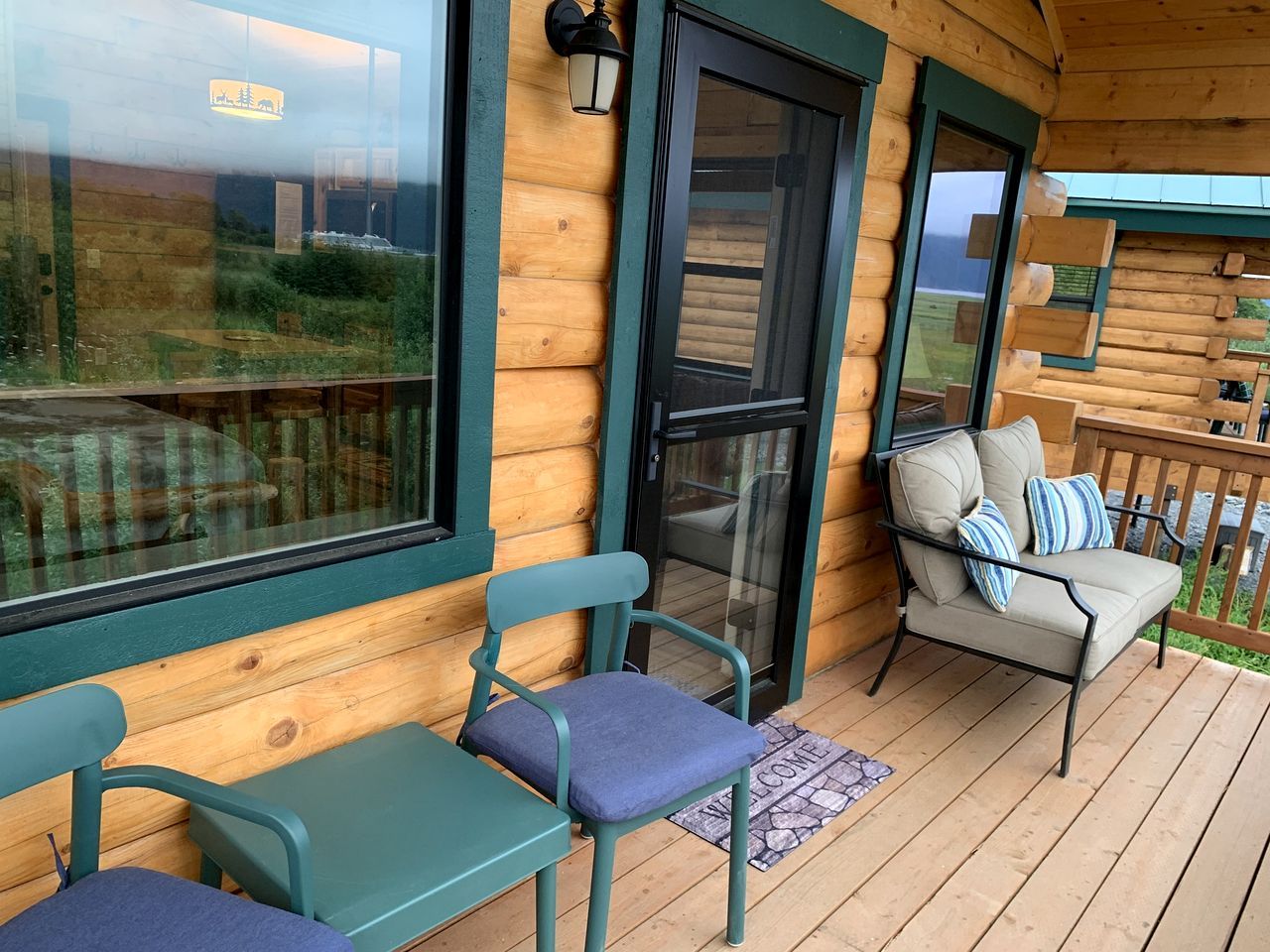 Een houten hut met een veranda, twee stoelen, een bank en een deurmat.