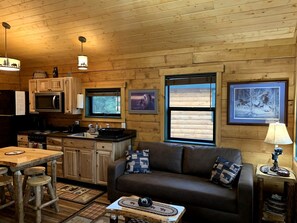 Ein gemütliches Blockhaus-Interieur mit Holzausstattung, einem Essbereich, einer Couch und einer Küche mit Mikrowelle und Herd.