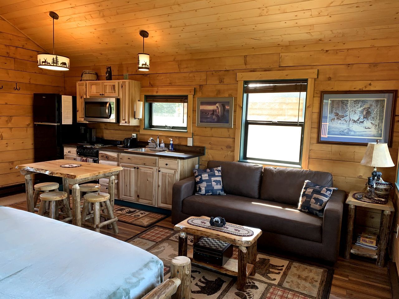 A cozy cabin interior with a wooden dining table, a sofa, and a kitchen area.