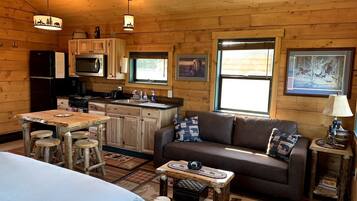 A cozy cabin interior with a wooden dining table, a sofa, and a kitchen area.