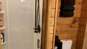 A wooden-paneled bathroom with a glass-enclosed shower, a toilet, and a shelf with toiletries.