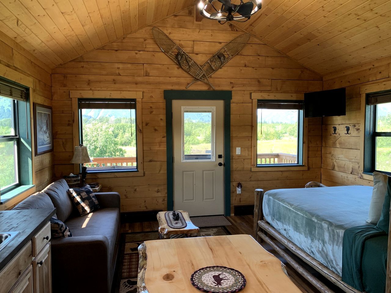Une cabane avec un intérieur en bois, un canapé, un lit, une table et un téléviseur.