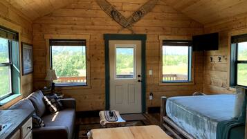 Une cabane avec un intérieur en bois, un canapé, un lit, une table et un téléviseur.