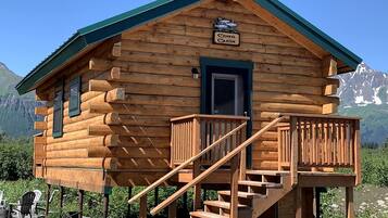 A wooden cabin with a sign reading 'Coho Cabin,' a staircase, and a view of mountains.