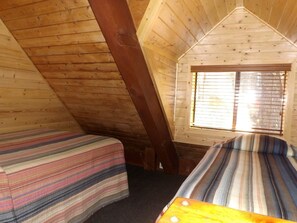 Une cabane avec deux lits, des murs en bois, un plafond en pente et une fenêtre avec des stores.