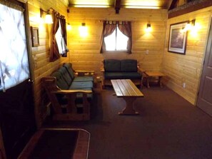 L’intérieur d’une cabane avec des murs en bois, un canapé vert, un banc en bois, une table et deux lampes fixées au mur.