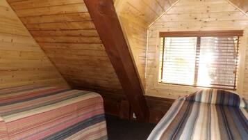 Une cabane avec deux lits, des murs en bois, un plafond en pente et une fenêtre avec des stores.
