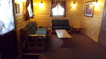 L’intérieur d’une cabane avec des murs en bois, un canapé vert, un banc en bois, une table et deux lampes fixées au mur.