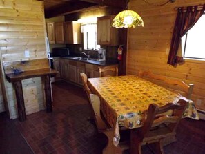 Un intérieur en bois comprenant une table à manger, des chaises, un coin cuisine et un luminaire suspendu.