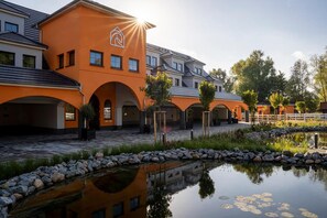 A modern building with a distinctive orange facade, multiple arches, and a reflective water feature in the foreground.