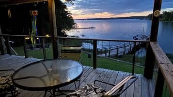 A covered outdoor deck with a table and chairs, overlooking a body of water.