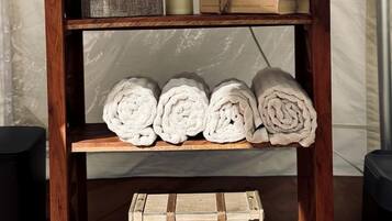 A wooden shelf with a white kettle, books, rolled towels, and a vintage suitcase.