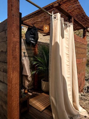 Une cabane en bois avec un espace douche, un sac suspendu et une plante en pot.