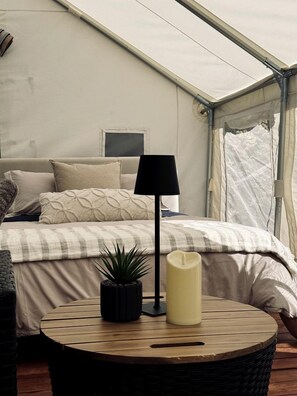 A tented room with a bed, a lamp, a candle, and a small plant.