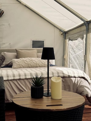 Una habitación con tienda de campaña, una cama, una lámpara, una vela y una planta pequeña.
