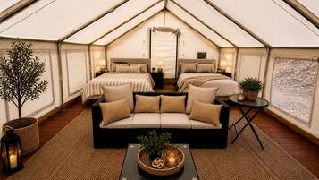 A tented accommodation with a sofa bed, a small table with a plant, and a lamp.