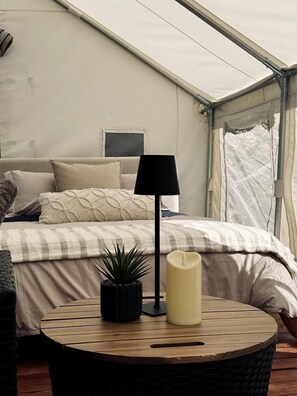 Una habitación con tienda de campaña, una cama, una lámpara, una vela y una planta pequeña.