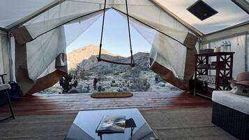 A tented room with a view of a mountainous landscape, a black table, and wicker furniture.