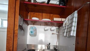 A compact kitchenette with a stainless steel stove, a sink, and a refrigerator. There are wooden cabinets above the stove and a small shelf with dishes. - Cozy Oceanfront Escape with Stunning Views in North Truro, Massachusetts (North Truro)