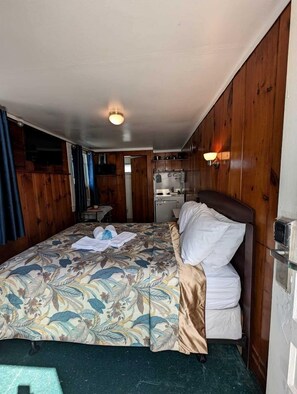 A compact room with a bed, a small kitchenette, and a door leading to another room. - Cozy Oceanfront Escape with Stunning Views in North Truro, Massachusetts (North Truro)