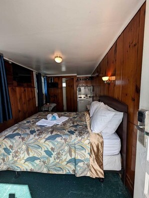 A compact room with a bed, a small kitchenette, and a door leading to another room. - Cozy Oceanfront Escape with Stunning Views in North Truro, Massachusetts (North Truro)