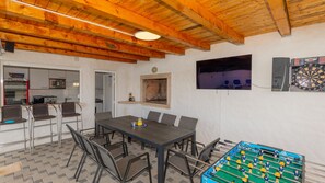 A dining area with a table and chairs, a foosball table, a dartboard, and a TV screen. - Villa Mili by Villas Guide (Nova Sela)