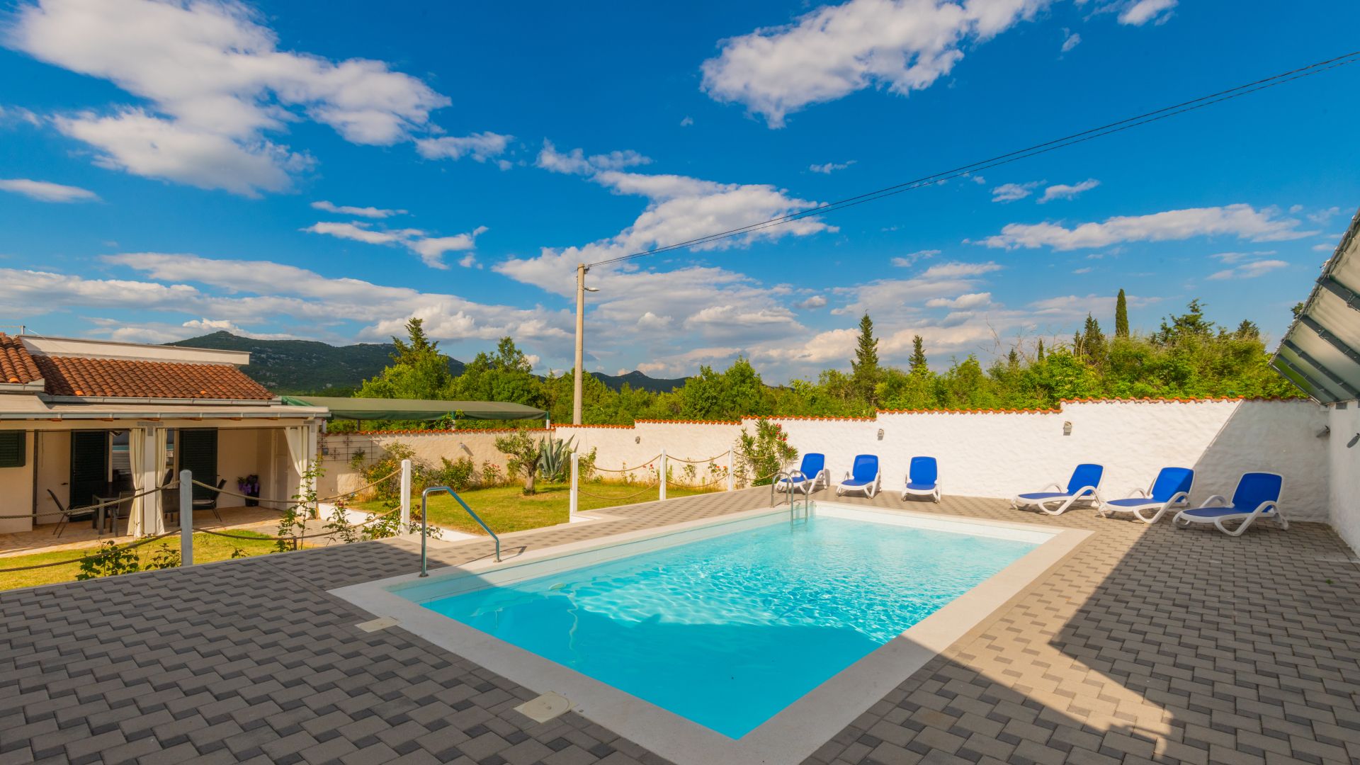 A swimming pool with lounge chairs, a covered patio, and a view of mountains.