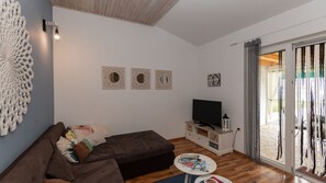 Ein Wohnzimmer mit einer Couch, einem Fernseher, Wanddekoration und einer Glasschiebetür, die zu einem Außenbereich führt.