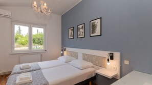 Ein Schlafzimmer mit zwei Betten, einer Chandelieber, gerahmten Bildern und einem Fenster mit Blick auf Grünflächen.