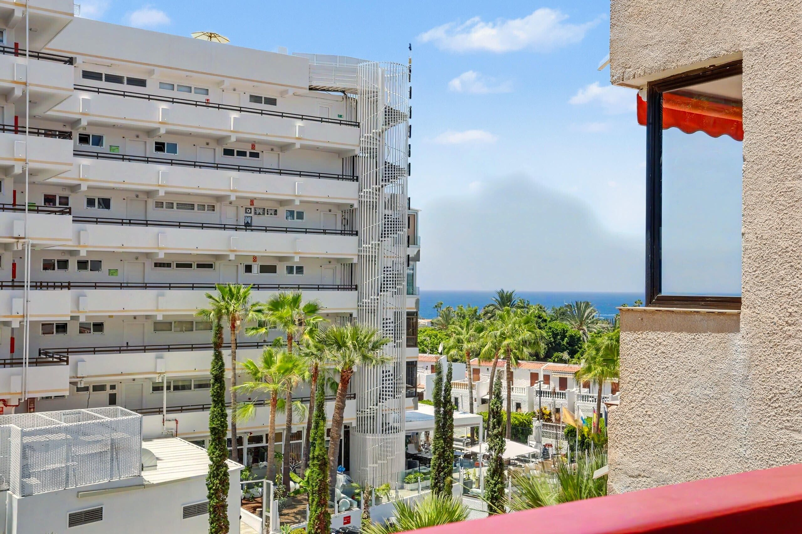 A multi-story hotel with balconies, a view of the sea, and palm trees.