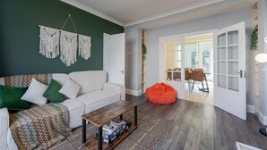 Un salon avec un canapé blanc, une table basse en bois, une décoration murale en macramé et un fauteuil en forme de poire rouge.