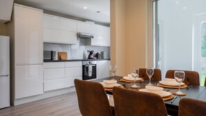 Une cuisine moderne avec des meubles blancs, une table à manger dressée pour six personnes et une grande fenêtre.