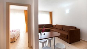 A room with a brown sofa, a small table, and a bed with a white cover. - Begonvil Apart Hotel (Antalya)