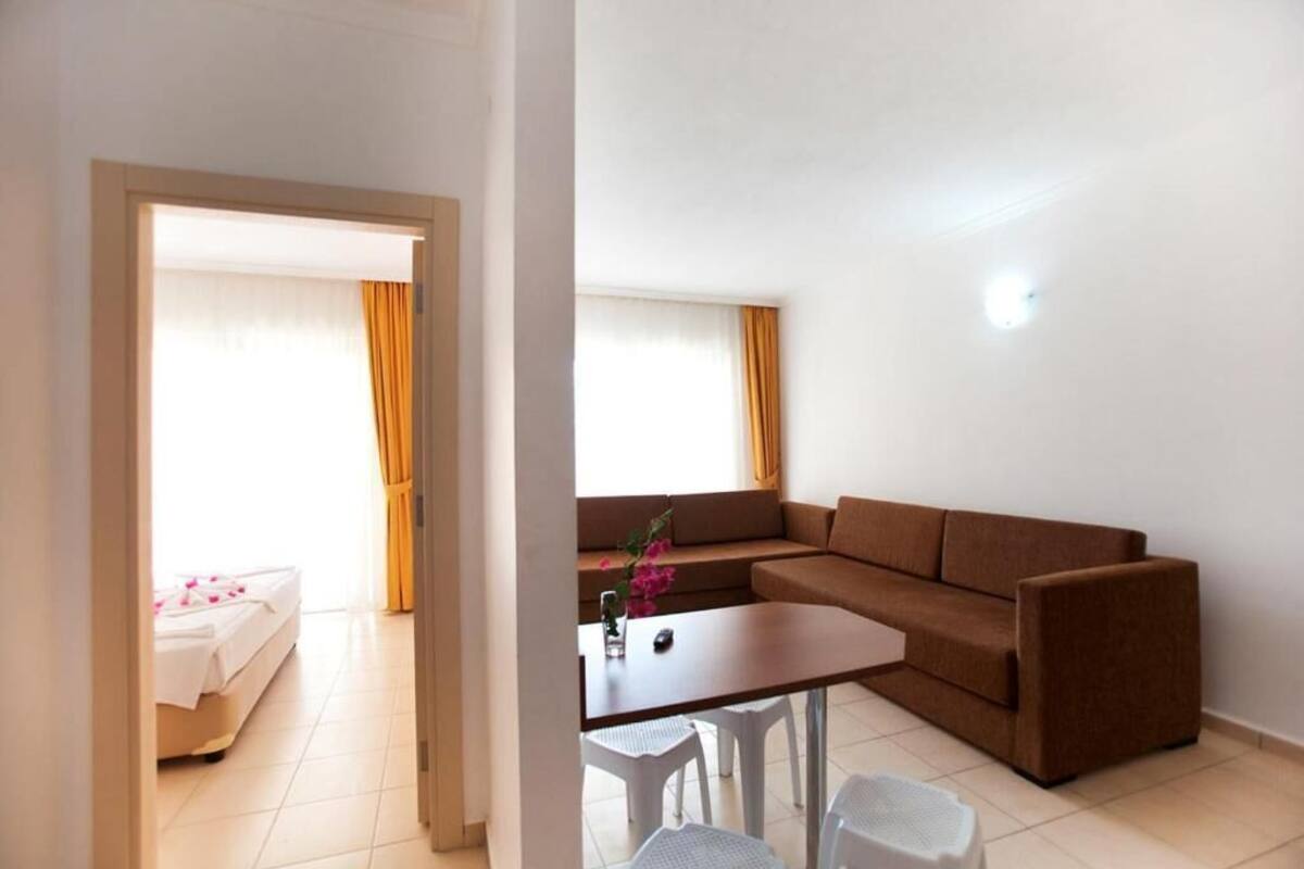 A room with a brown sofa, a small table, and a bed with a white cover.