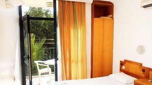 A bedroom with a bed, a wooden wardrobe, a small table, and a chair. - Begonvil Apart Hotel (Antalya)