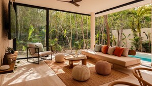 A modern living room with a sofa, chairs, and a coffee table, large windows, and a ceiling fan. - Villa Lumila Rooftop Sunset & Jungle Views (Tulum)