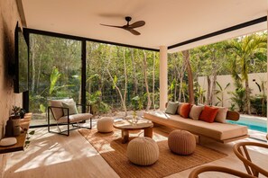 A modern living room with a sofa, chairs, and a coffee table, large windows, and a ceiling fan. - Villa Lumila Rooftop Sunset & Jungle Views (Tulum)