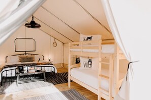 A cozy tent-style room with a bunk bed, a desk with a chair, and a hanging light fixture.
