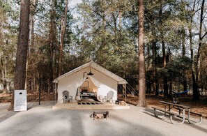 A tented camping area with a picnic table, chairs, and a hammock.