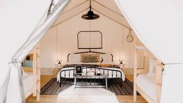 Une pièce aménagée avec une tente, un lit, un luminaire suspendu et une petite table.