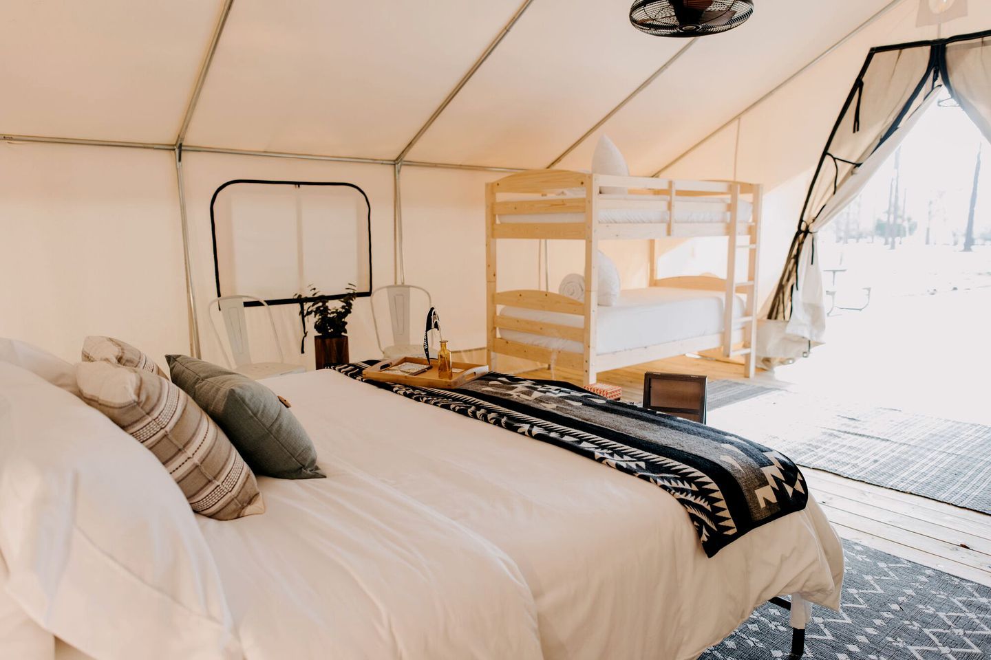 A tented room with a bed, a chair, a table with a tray, and a laptop.
