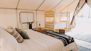 A tented room with a bed, a chair, a table with a tray, and a laptop.