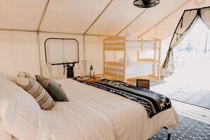 Um quarto coberto por uma tenda, com uma cama, uma cadeira, uma mesa com um tabuleiro e um computador portátil.