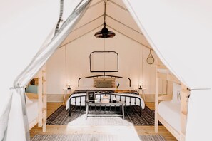 A tented room with a bed, a hanging light fixture, and a small table. - Luxury Glamping by Lake Blackshear: Cozy Safari Tent in Cordele, Georgia (Cordele)