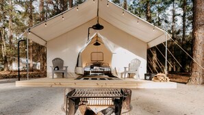 Una tenda con un letto, sedie e un braciere immersa in un bosco.