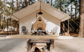 A tent with a bed, chairs, and a fire pit in a forest setting. - Luxury Glamping by Lake Blackshear: Cozy Safari Tent in Cordele, Georgia (Cordele)