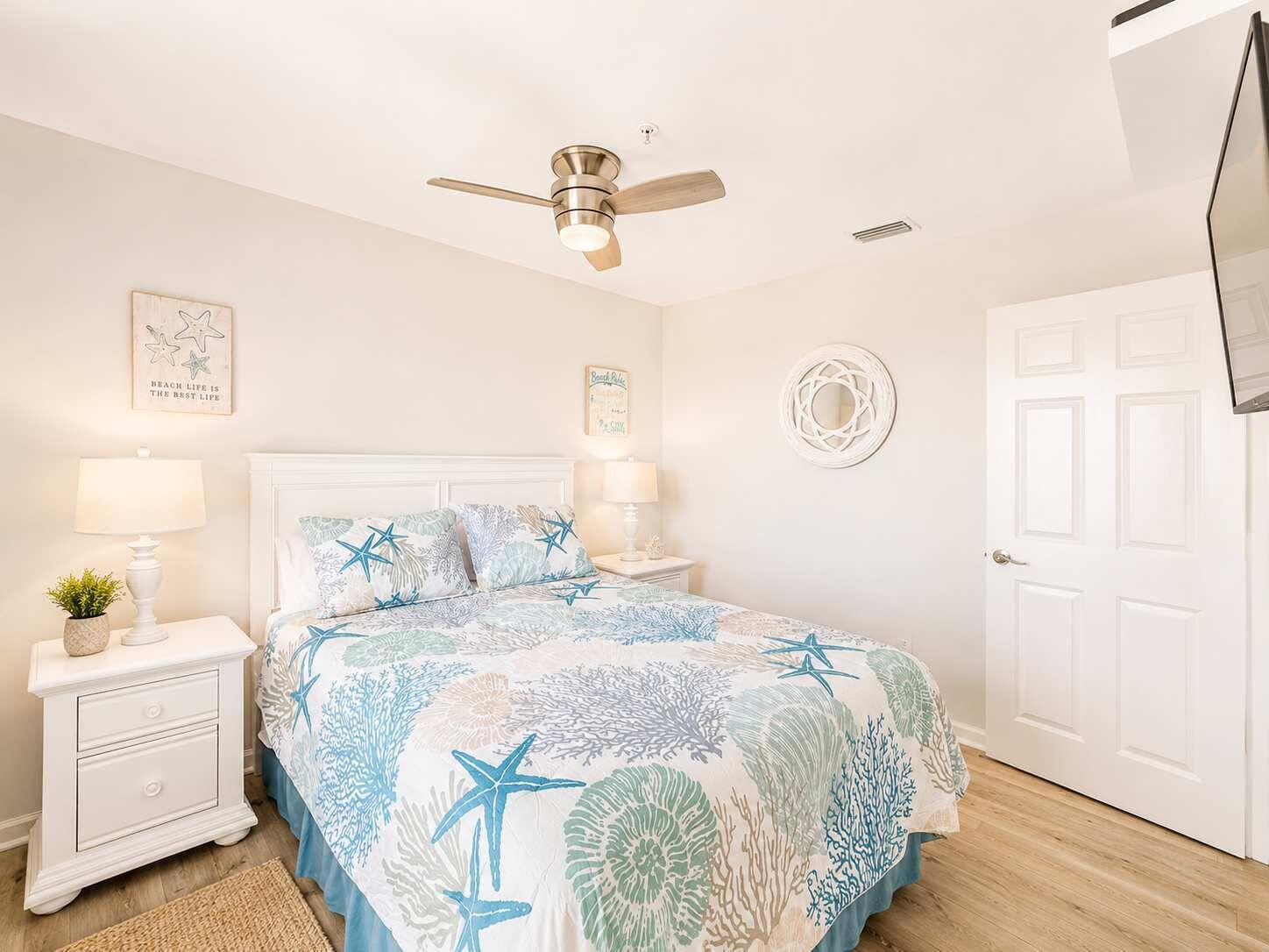 Une chambre à coucher comprenant un lit, des tables de chevet, un ventilateur de plafond, des éléments de décoration murale et une porte.